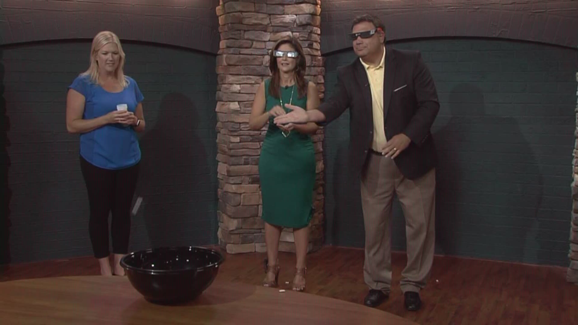 Beth and Russell try to shoot eclipse gum into a bowl while wearing eclipse glasses.